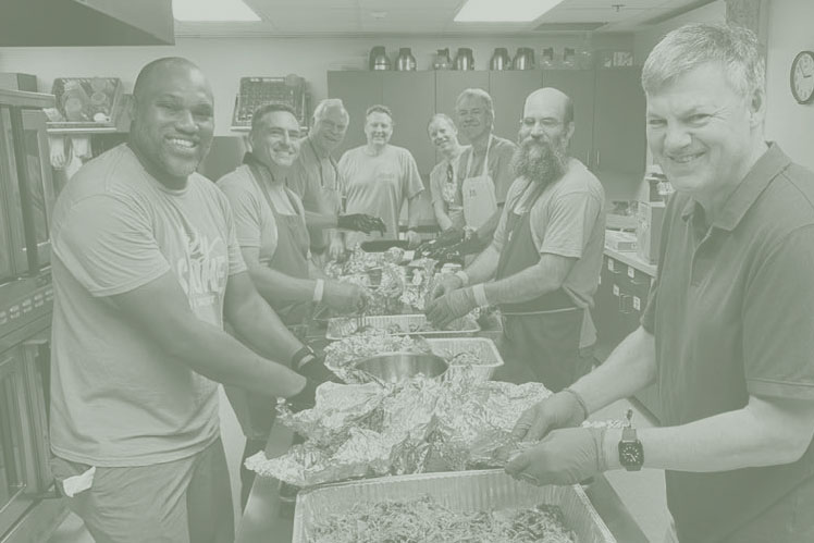Eight men stand around a table in Christ UMC's kitchen, shredding pork BBQ for Holy Smokes.