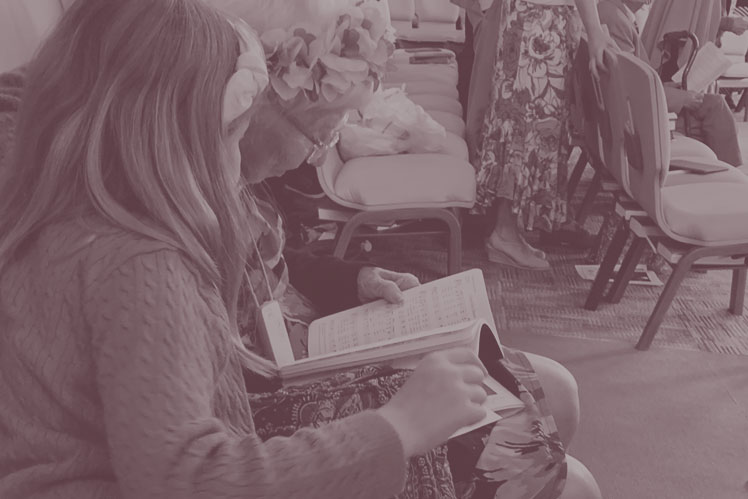 Young worshipper shares hymnal with senior during worship at Christ UMC,