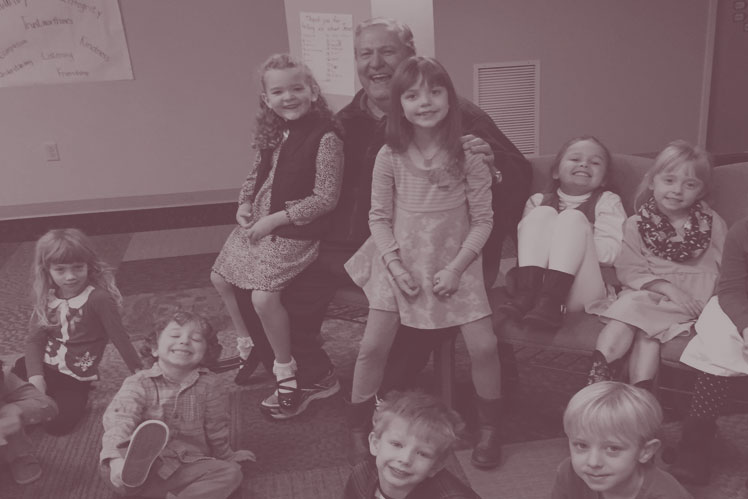 A Christ UMC Children's Sunday School teacher sits surrounded by smiling children in the Children's Commons area at Christ UMC.