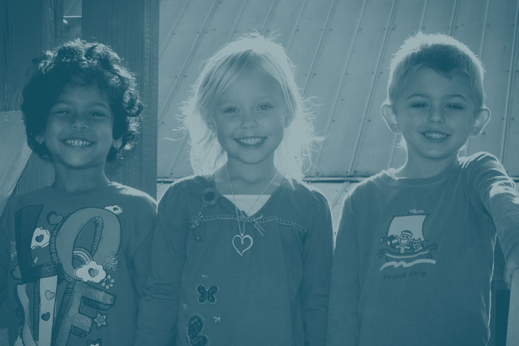 Three children smile while playing on playground equipment at Christ UMC in Franklin, TN.